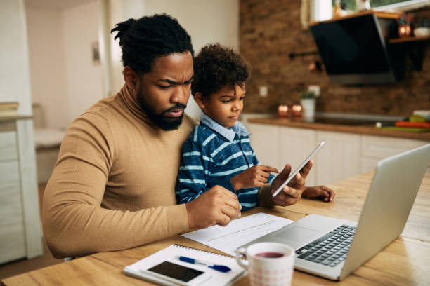 istock Black stay at home father working on laptop while his small son is using touchpad at home. 1287923584