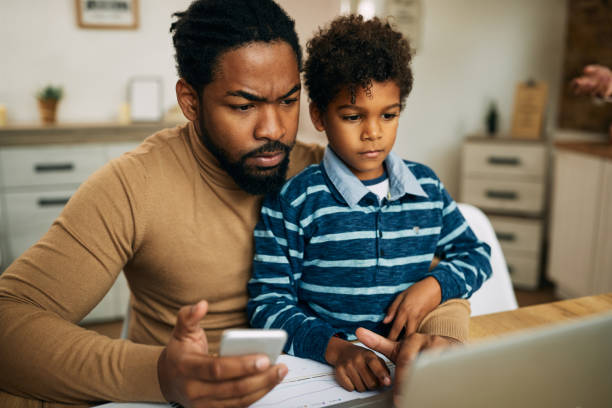 istock African American stay at home father using phone while working on laptop. 1287923706