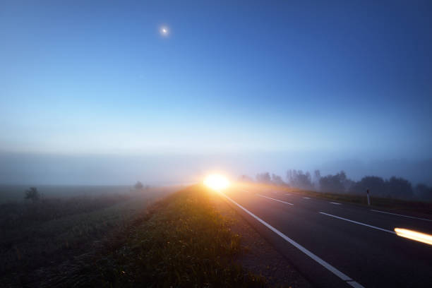 Panoramic view of the empty highway through the fields in a fog at night. Moonlight. Sunrise. Europe. Transportation, logistics, travel, road trip, freedom, driving. Motion blur effect. Rural scene