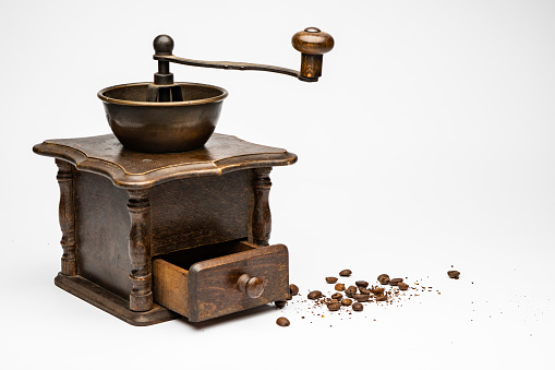 Old manual coffee grinder. Brick wall as a background with scattered coffee beans on the table