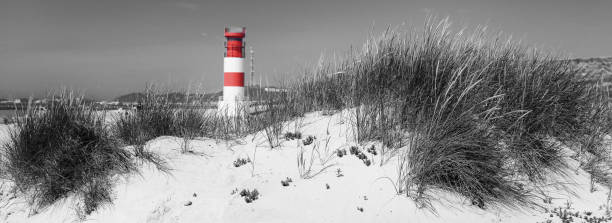 istock Red and white striped lighthouse on sand dunes. Selective color in black and white, 1287927093