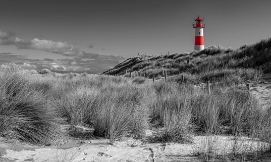Red and white striped lighthouse on sand dunes. Selective color in black and white,