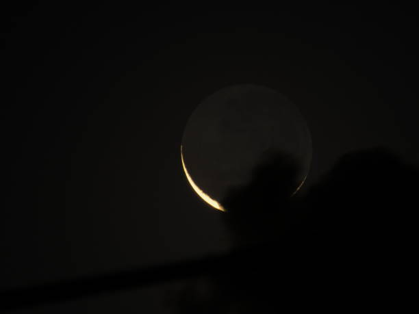 istock new moon, with its dark side illuminated by the gray light, partially covered by dark clouds in a black sky. 1287930126