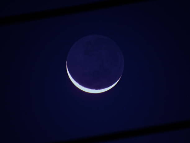 istock new moon, with its dark side illuminated by the gray light, under a bluish black sky. 1287930375