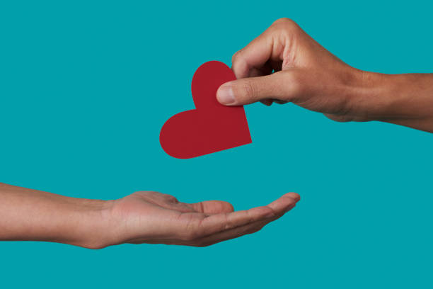 person giving a heart to another person a person giving a red heart to another person on a blue background altruism photos stock pictures, royalty-free photos & images