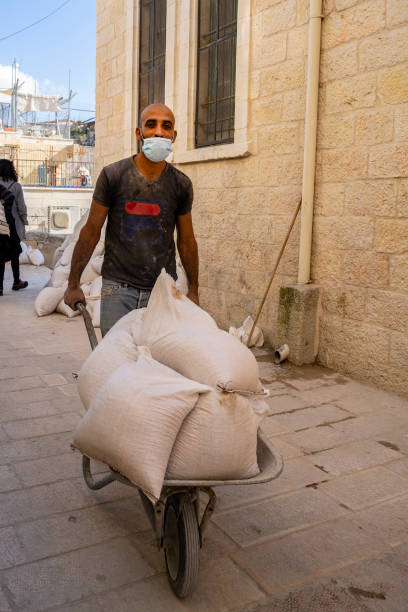 A Construction Worker Jerusalem, Israel - November 21st, 2020: A construction worker, wearing a protective mask, pushing a wheelbarrow full of building materials in old Jerusalem, Israel. sack barrow stock pictures, royalty-free photos & images