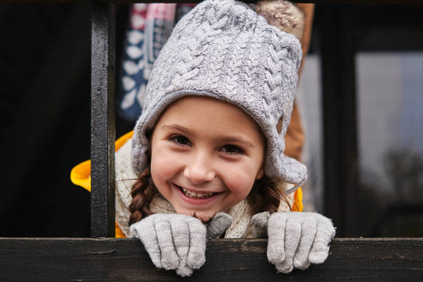 Adorable playful little girl in raincoat and with gray hat and gloves having a fun time during vacation with her parents