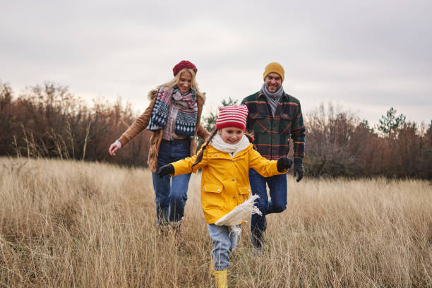 fröhliche tochter läuft an einem weihnachtsmorgen mit ihren eltern durch die wiese - family fun running couple stock-fotos und bilder
