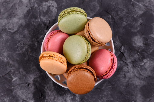 Top view of bowl with colorful French macaron sweets on dark background