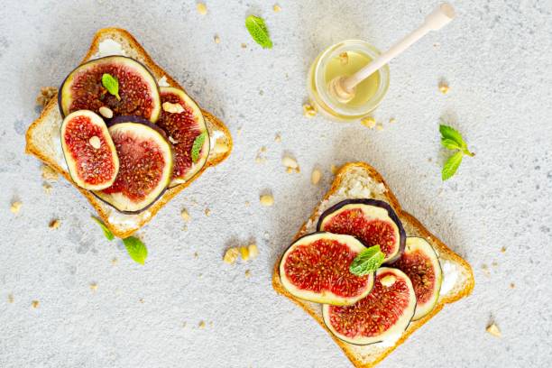 istock Crispy bruschetta with soft ricotta, ripe figs, walnuts and pine nuts, mint and honey on a light background. Figs fruit toast on marble table with honey and walnut. Top View. 1287944971