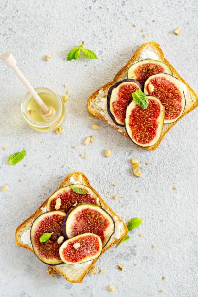 istock Crispy bruschetta with soft ricotta, ripe figs, walnuts and pine nuts, mint and honey on a light background. Figs fruit toast on marble table with honey and walnut. Top View. 1287945040