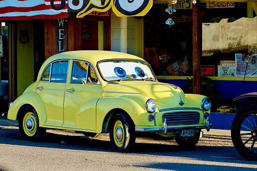 Seligman, Arizona, USA - July 30, 2020: A brightly painted yellow classic Morris Minor 1000 car with “eyes” parked along historic Route 66 in downtown Seligman, Arizona.