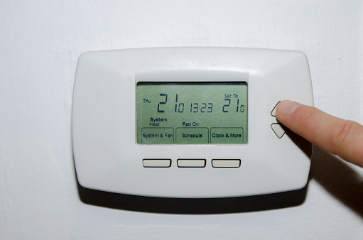 Digital thermostat on white background with finger on a button to set