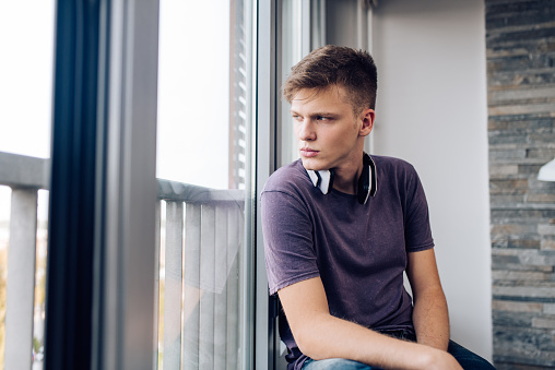 Portrait of a young man sitting by the window alone at home.