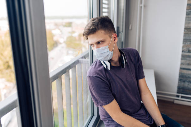 istock Young man with a face mask leaning on the window and looking sadly 1287950077