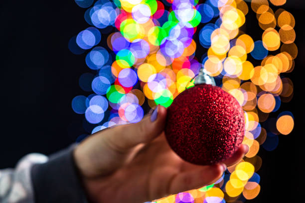 istock Holding Christmas bauble decoration isolated on background with blurred lights. December season, Christmas composition. 1287950782