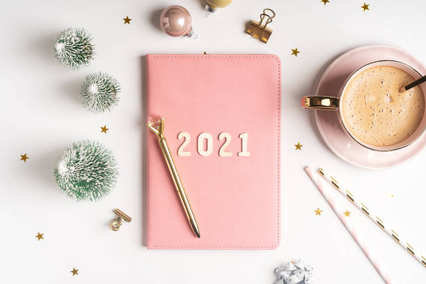 istock Desktop Christmas notepad with 2021 letters text. Flat lay of white table background with planner, cup of coffee, Christmas decoration and stationery 1287951141