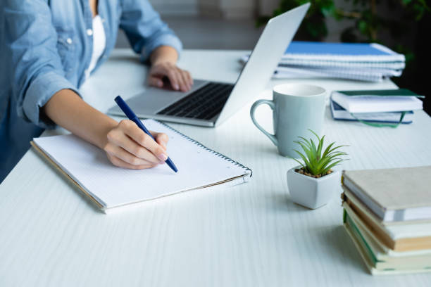 istock cropped view of woman making notes in notebook and typing on laptop 1287961150