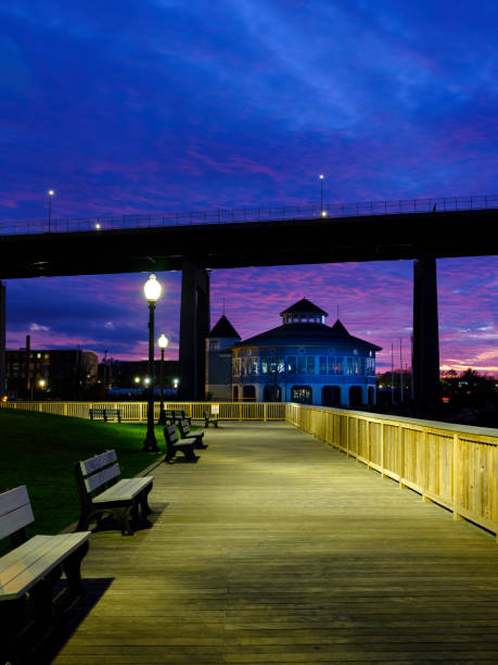 istock Nightscape of River Boardwalk with View of Silhouette Bridge 1287964587