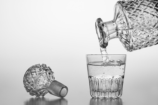 Pouring sparkling water from a carafe into a small glass. Decorative containers for serving water and alcohol. Light background.