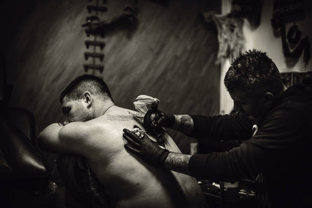 Tattoo artist tattooing a man's back in his tattoo studio.