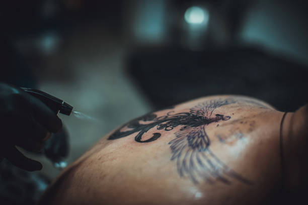 Tattoo artist applying alcohol to customers back tattoo. Disinfection during tattooing.