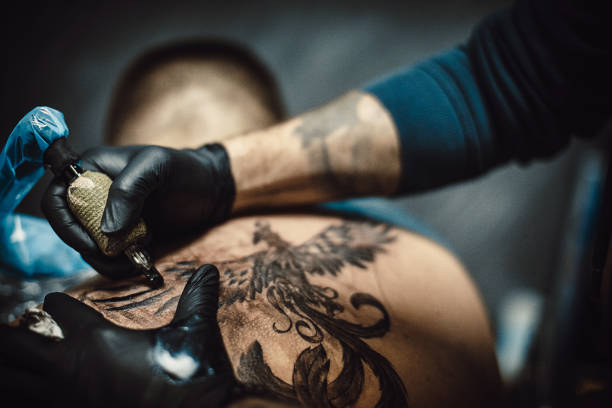 Tattoo artist tattooing a man's back in his tattoo studio.