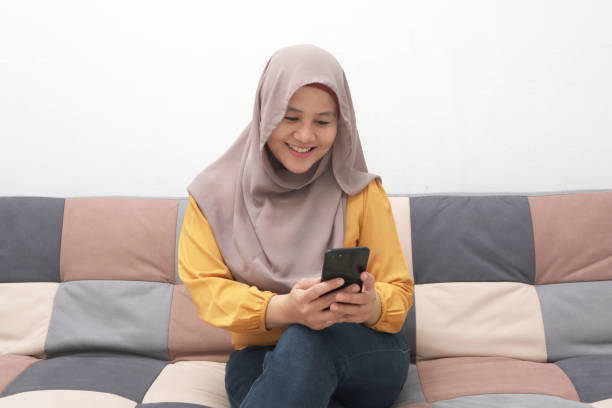 istock Beautiful Asian muslim woman using phone while sitting on sofa, girl doing chat message on smartphone and smiling 1287982763