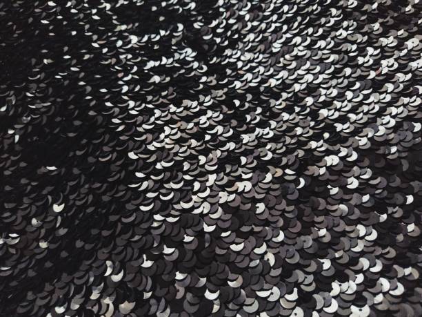 istock Sequin fabric. Black sequins with white and gray sheen. Reflection of light on individual elements in a chaotic manner. Sewing or Christmas decorative background 1287983539