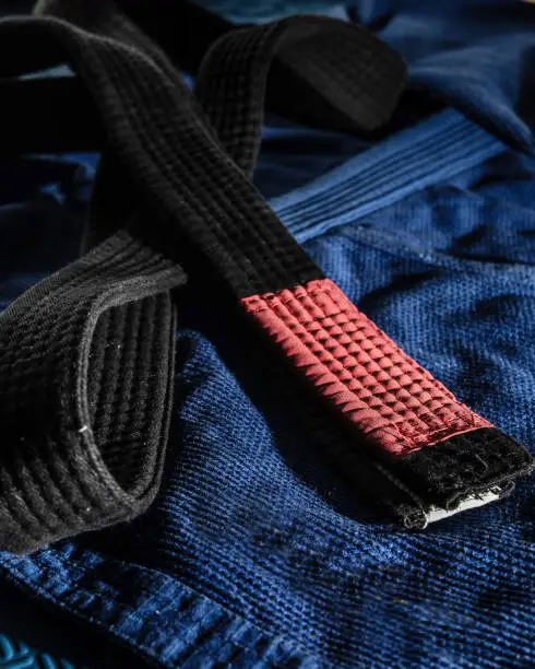 Close up on brazilian jiu jitsu bjj black belt on the blue kimono gi on tatami mats - martial arts grappling and training concept dark and high contrast filter