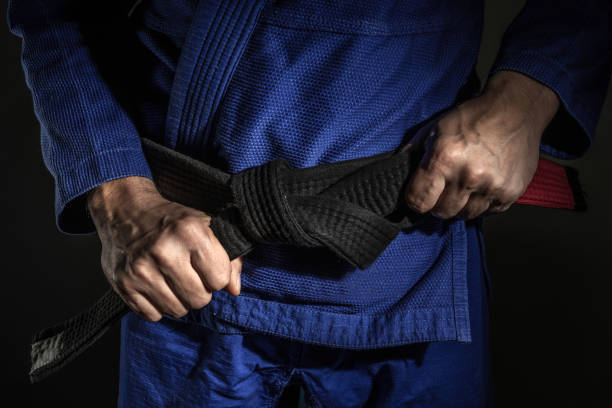 de cerca a mano de hombre caucásico desconocido sosteniendo brasil jiu jitsu bjj cinturón negro alrededor de su cintura mientras usa kimono gi en la oscuridad - habilidad de dominio de las artes marciales y concepto de logro de confianza - white collar worker fotografías e imágenes de stock