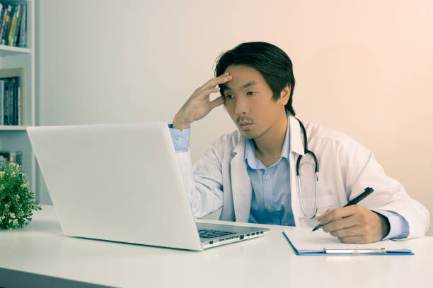 istock Serious Asian Doctor and Stethoscope Write Report and Using Laptop Computer in Vintage Tone 1288000823