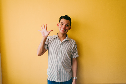 A happy young man waves at the camera. Isolated on a orange background.