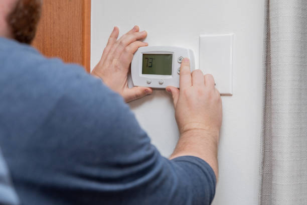 istock Man is pushing buttons and adjusting thermostat to change temperature at home 1288033790