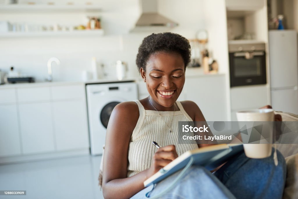 When you're at peace everything falls into place Shot of a young woman having tea and writing in a notebook on the sofa at home Diary Stock Photo