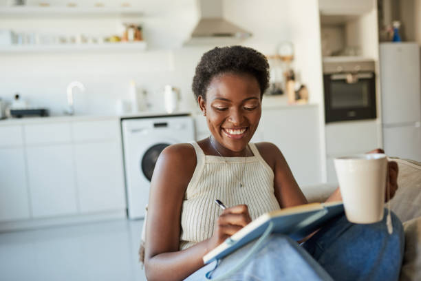 When you're at peace everything falls into place Shot of a young woman having tea and writing in a notebook on the sofa at home diary stock pictures, royalty-free photos & images