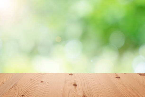 istock Empty wooden table top with blurred defocus natural green bokeh background, aesthetic creative design 1288035221