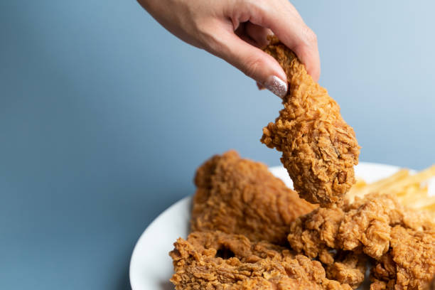 istock Hand holding drumsticks, crispy fried chicken in white plate on blue background. 1288035410