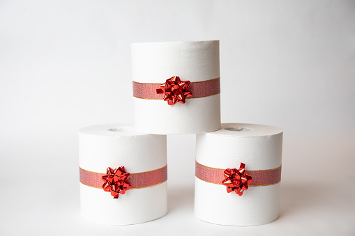 Rolls of toilet paper stacked and wrapped with Christmas ribbon on a white background.