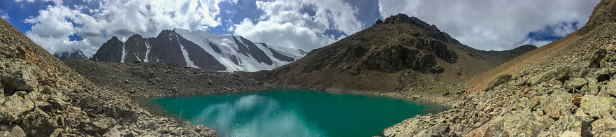 Panoramic view on glacial lake with turqoise water in Altai mountains in summer with cloudy sky.