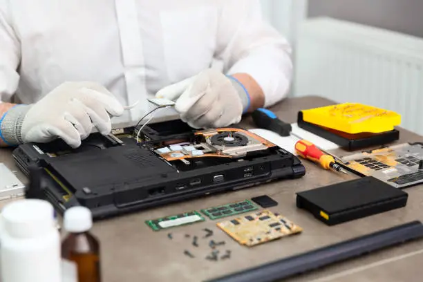 Laptop computer parts and various work tools are on the table and hands of a technician holding tweezers and wi-fi module.