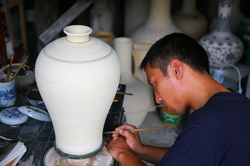 Jingdezhen, China - June 29, 2008: A worker painting and decorating a porcelain jar at ancient ceramic Kiln in Jingdezhen, Jiangxi, China