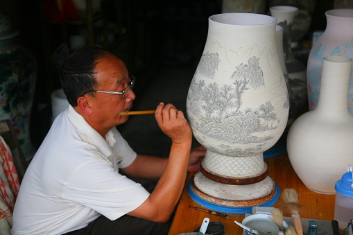 Jingdezhen, China - June 29, 2008: A worker painting and decorating a porcelain vase at ancient ceramic Kiln in Jingdezhen, Jiangxi, China