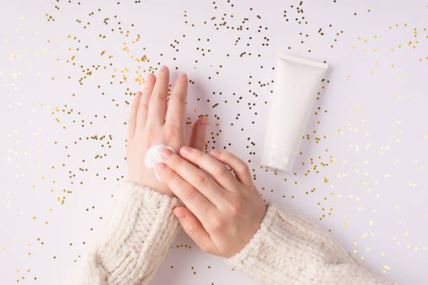 mit feuchtigkeitsbefeuchtender sahne auf wintersaison konzept.  top flatlay overhead über nahaufnahme foto von weiblichen mädchen hände schmieren weiße glatte creme auf glänzenden hintergrund - jar human hand moisturizer packaging stock-fotos und bilder