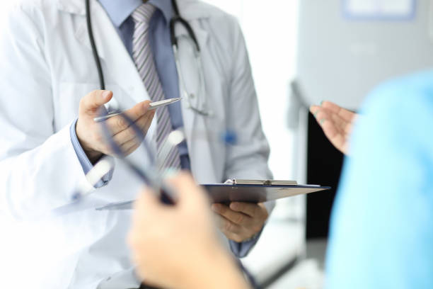 istock Doctor with phonendoscope holds pen and folder with documents in closeup conversation with another doctor 1288051829
