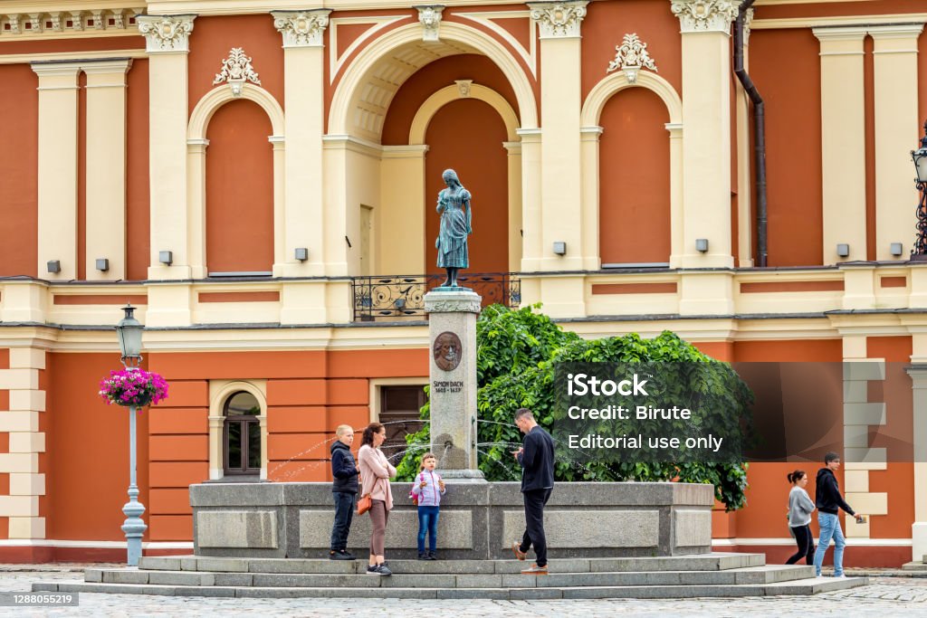 Memorial of poet Simon Dach and Taravos Anike (Annchen von Tharau) in Theatre square of Klaipeda, Lithuania Klaipeda, Lithuania - July 10, 2020: Tourists at the memorial of Simon Dach and Taravos Anike (Annchen von Tharau) in Theatre square. Created by A. Kunne (1912), restored by M. Hacke (1989). Architecture Stock Photo Memorial of poet Simon Dach and Taravos Anike (Annchen von Tharau) in Theatre square of Klaipeda, Lithuania Klaipeda, Lithuania - July 10, 2020: Tourists at the memorial of Simon Dach and Taravos Anike (Annchen von Tharau) in Theatre square. Created by A. Kunne (1912), restored by M. Hacke (1989). Architecture Stock Photo
