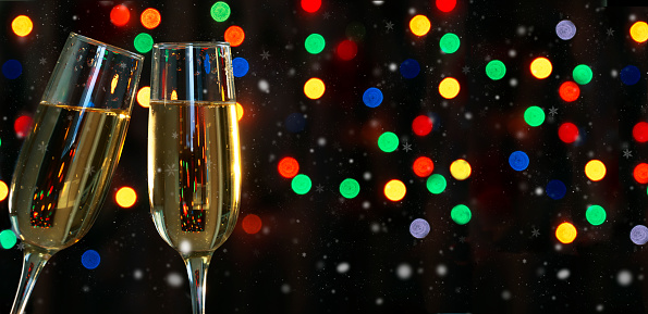 Two champagne glasses on a dark background with a colored garland bokeh.