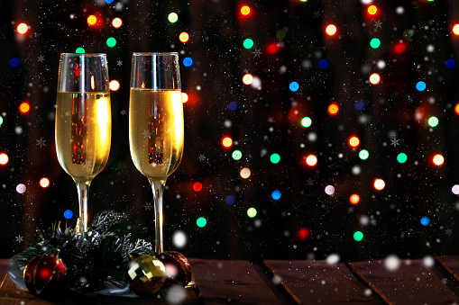 Two champagne glasses and Christmas decorations on the table on a dark background with a colored garland bokeh.