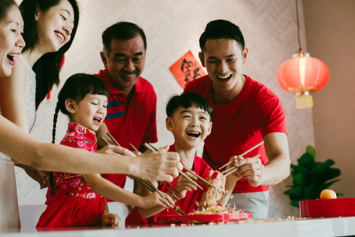 Image of Happy Asian Chinese family tossing of Yee Sang or Yu Sheng with raw salmon fillet traditional Chinese New Year prosperity delicacies.
