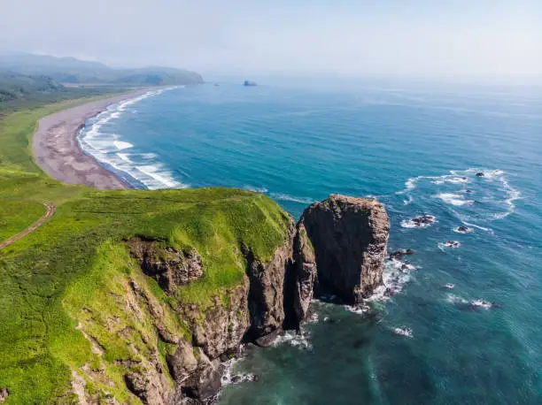Halaktyr beach. Kamchatka. Russian federation. Dark almost black color sand beach of Pacific ocean. Stone mountains and yellow grass are on a background. Light blue sky.